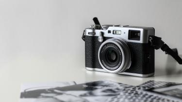 An old school black and silver hand held camera against a grey background